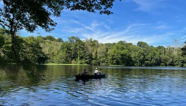 Une rivière calme qui coule au milieu de la verdure. On aperçoit une barque au milieu de l'eau avec deux occupants. Font valley, gîtes à la ferme.